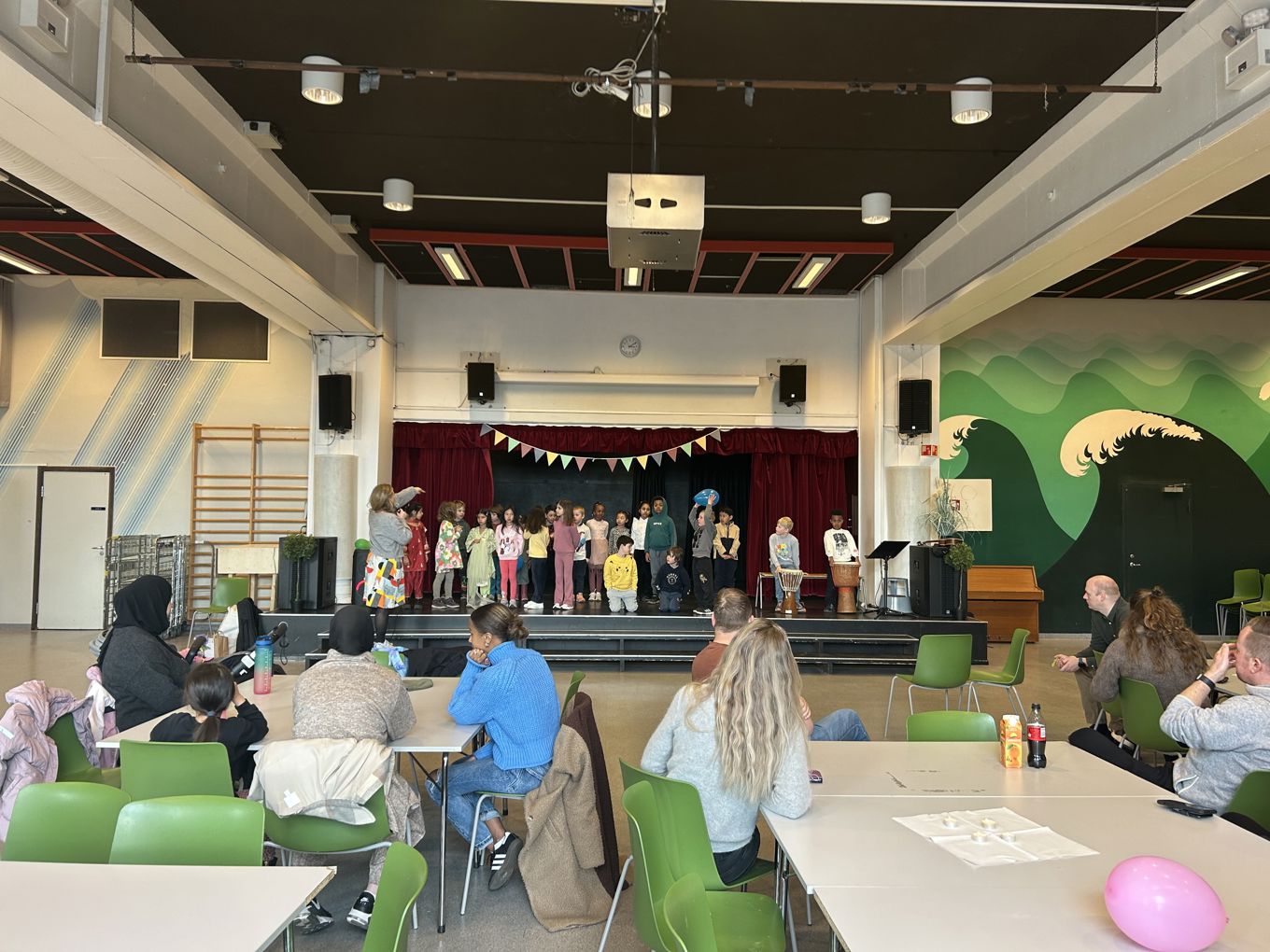 en gruppe mennesker som sitter i et rom med en scene og en stor skjerm