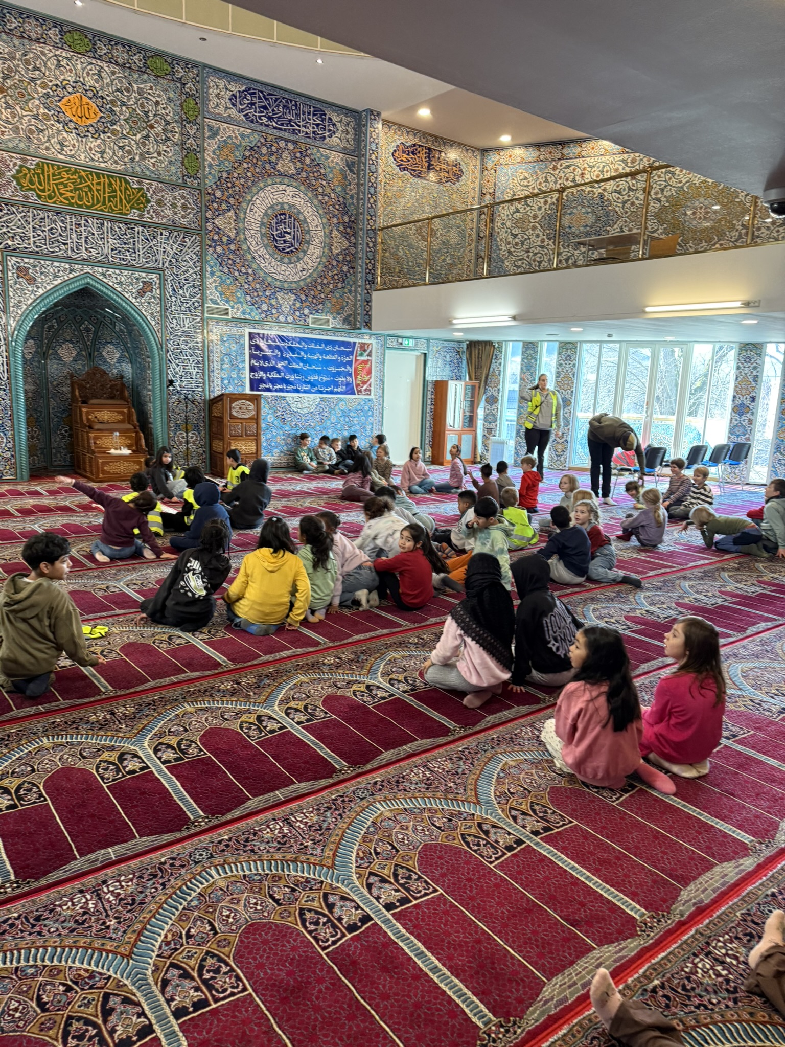 en gruppe mennesker som sitter på gulvet i et rom med en stor rød løper