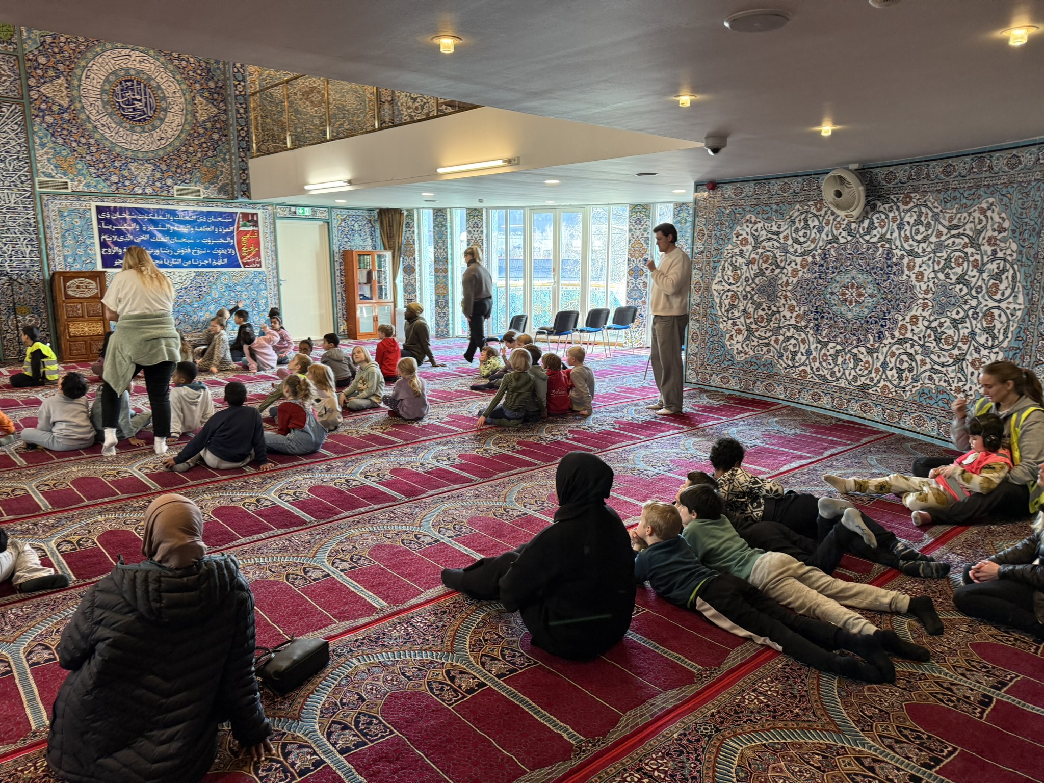 en gruppe mennesker som sitter på gulvet i et rom med en person stående og en person stående