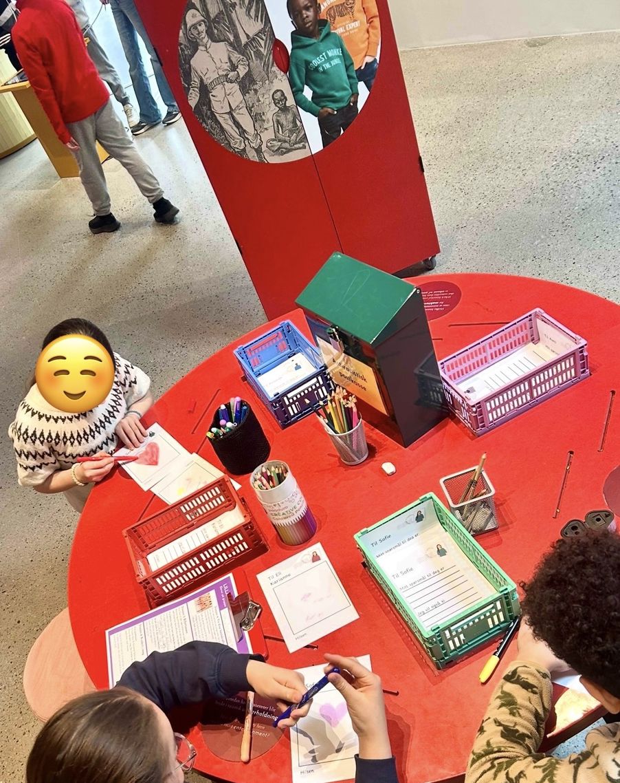 En gruppe mennesker som sitter rundt et bord med bøker og en tegneseriefigur